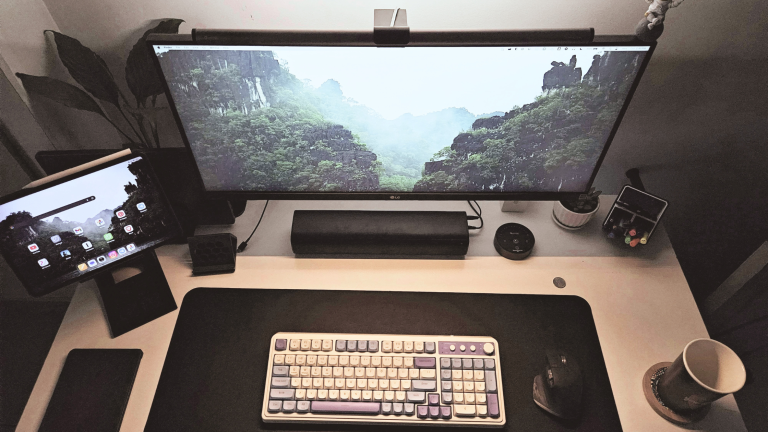 A working desk cleared down to a screen, lamp, water, pen holder and notebook