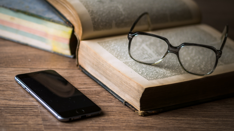 an open book next to a phone turned face down on a desk in the evening